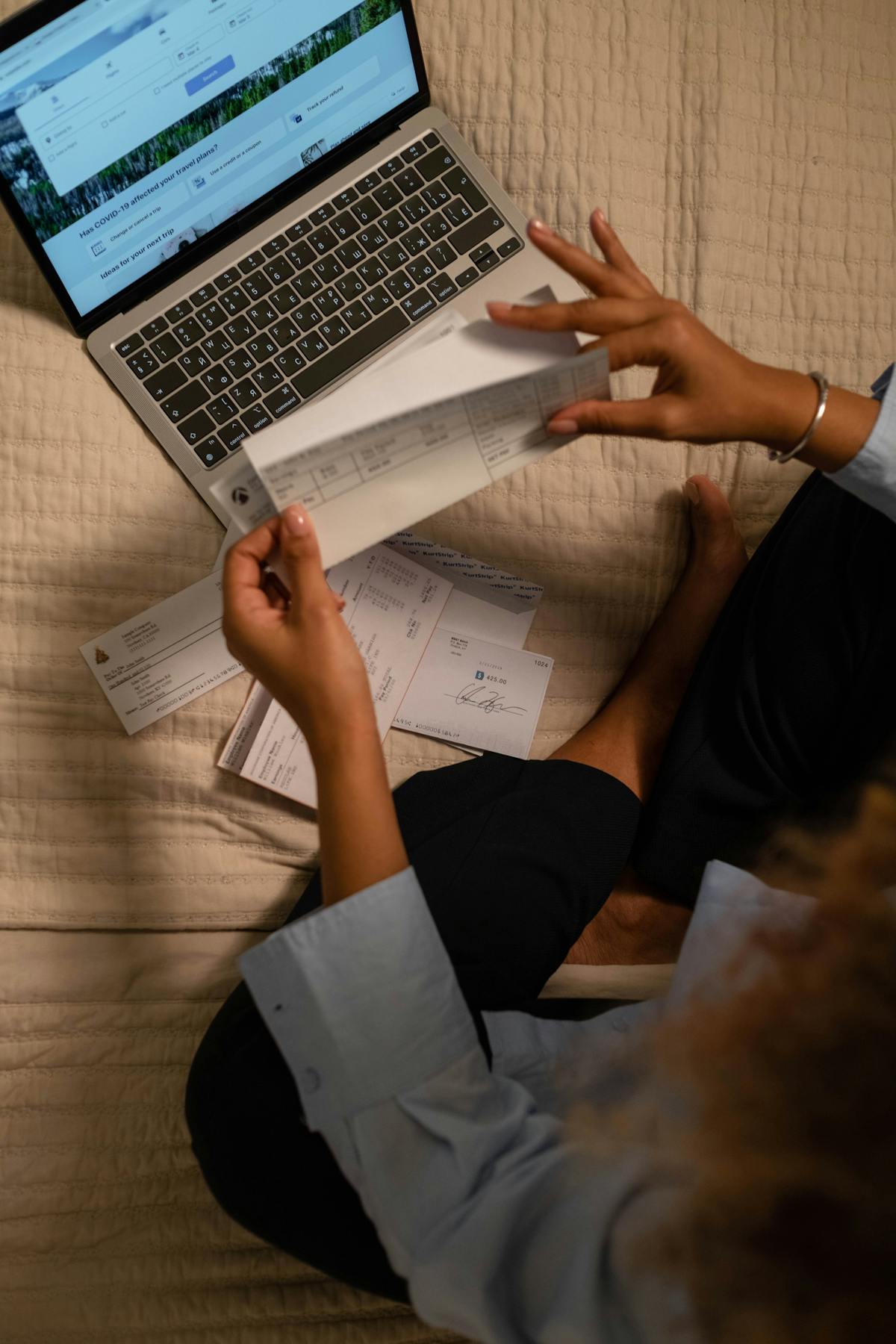 Documentos y cheques sobre una cama junto a una laptop